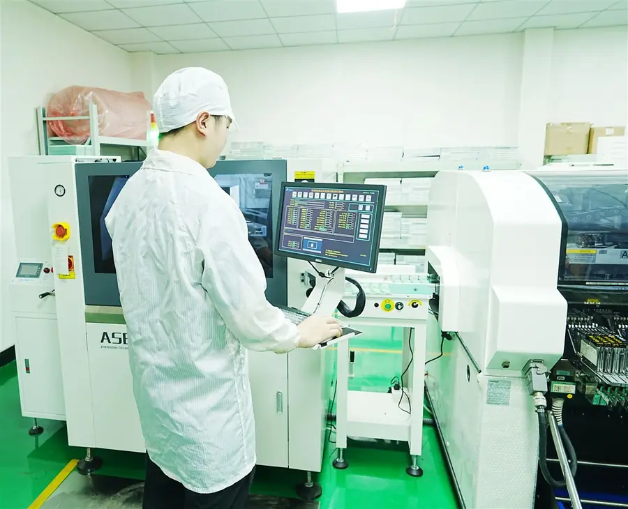 Operator in an anti-static suit at the automatic solder paste printer next to the pick-and-place machine